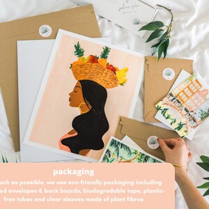 May include: A close-up of a brown paper envelope with a sticker featuring a green palm tree. The envelope is on a white surface with a printed art print of a woman with a basket of fruit on her head. The text "packaging" is printed in white on a peach background.