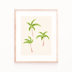 May include: A framed watercolor print featuring three palm trees. The palm trees have green fronds and brown trunks, set against a cream-colored background. The frame is made of light-colored wood, adding a natural touch to the artwork.