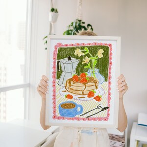 K&ouml;nnte beinhalten: Gerahmte Buntstiftzeichnung einer Fr&uuml;hst&uuml;cksszene. Das Kunstwerk zeigt Pfannkuchen mit Erdbeeren, eine Kaffeetasse, eine Kaffeekanne und eine Vase mit Blumen. Der Rahmen ist wei&szlig;, und die Zeichnung hat einen rosa-gr&uuml;nen Rand.