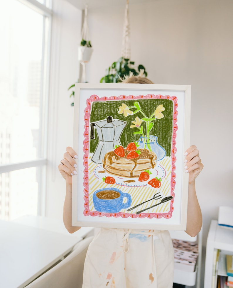 K&ouml;nnte beinhalten: Gerahmte Buntstiftzeichnung einer Fr&uuml;hst&uuml;cksszene. Das Kunstwerk zeigt Pfannkuchen mit Erdbeeren, eine Kaffeetasse, eine Kaffeekanne und eine Vase mit Blumen. Der Rahmen ist wei&szlig;, und die Zeichnung hat einen rosa-gr&uuml;nen Rand.