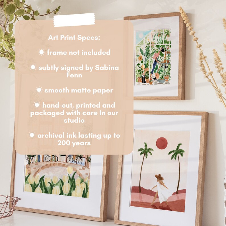 Op de afbeelding: Drie ingelijste kunstprints met een witte achtergrond. De print links toont een kleurrijke illustratie van een tuin met tulpen. De print in het midden toont een kleurrijke illustratie van een kas met een persoon die planten verzorgt. De print rechts toont een kleurrijke illustratie van een persoon die in een woestijnlandschap met palmbomen en een rode zon loopt. De tekst aan de linkerkant van de afbeelding luidt "Art Print Specs: frame not included subtly signed by Sabina Fenn smooth matte paper hand-cut, printed and packaged with care in our studio archival ink lasting up to 200 years"