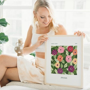 Puede incluir: Un cuadro enmarcado con un dise&ntilde;o floral de zinnias. La obra de arte presenta un patr&oacute;n de flores rosas, rojas, naranjas, amarillas y moradas con hojas verdes sobre un fondo verde oscuro. La impresi&oacute;n est&aacute; etiquetada como "ZINNIA" y "SABINA FEHN".