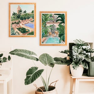 K&ouml;nnte beinhalten: Zwei gerahmte Aquarelle von Au&szlig;enmotiven mit Swimmingpools. Die Bilder h&auml;ngen an einer wei&szlig;en Wand mit einer Topfpflanze davor.