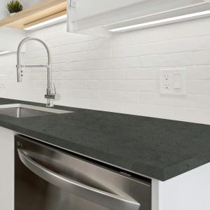 May include: A modern kitchen countertop with a dark gray surface. The countertop is paired with a stainless steel dishwasher and a stainless steel faucet. White subway tile backsplash and white cabinets complete the kitchen design.