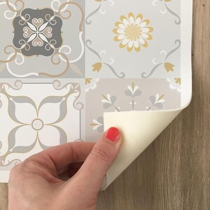 Op de afbeelding: Een rol zelfklevende tegelcontactpapier met een grijs en wit bloemenpatroon. Het papier wordt teruggetrokken om de kleefrug te onthullen.