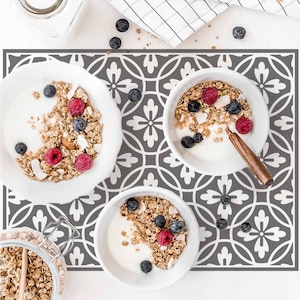 Op de afbeelding: Drie kommen yoghurt met granola, blauwe bessen en frambozen op een grijs en wit gepatroneerd placemat.