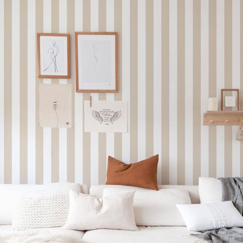 May include: A white sofa with brown and white cushions in front of a wall with vertical beige and white stripes. There are three framed prints on the wall, one with a line drawing of a person, one with a line drawing of wings, and one with the text "You are my everything".