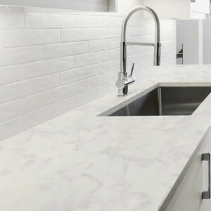 May include: A stainless steel high-arc kitchen faucet positioned over a rectangular sink basin. The countertop features a white marble pattern, and the wall is covered in white rectangular subway tiles with a glossy finish.