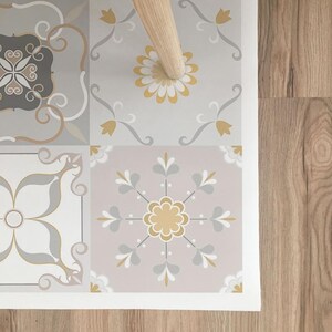 Op de afbeelding: Een vinyl vloermat met een herhalend patroon van grijze, witte en gele tegels. De tegels hebben verschillende bloem- en geometrische ontwerpen.