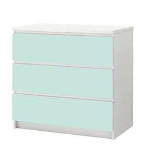 Op de afbeelding: Een witte commode met drie lades. De lades zijn lichtblauw.