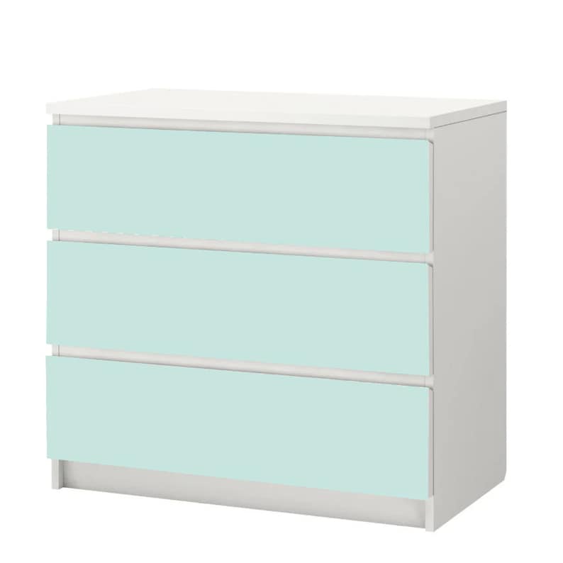 Op de afbeelding: Een witte commode met drie lades. De lades zijn lichtblauw.