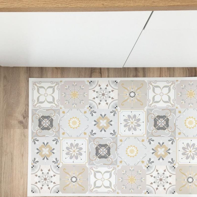 Op de afbeelding: Een gepatroneerd keukenkleed met een geometrisch ontwerp in grijstinten, beige en geel. Het kleed is gemaakt van individuele tegels met bloem- en geometrische patronen.