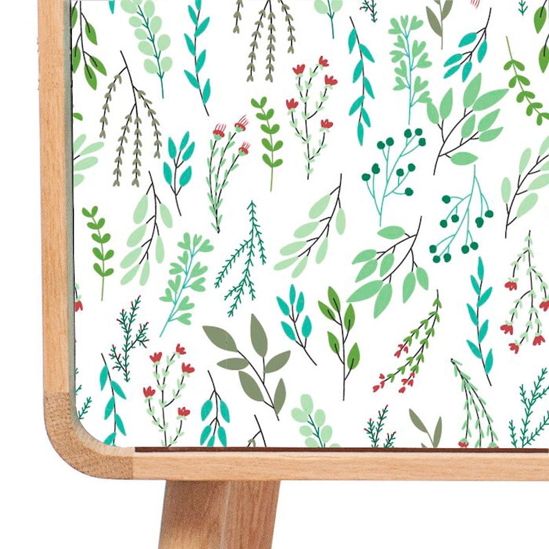 May include: A wooden cabinet with a white surface featuring a repeating pattern of green and blue leaves and red flowers. The cabinet has a light wood finish and four legs.