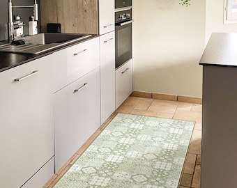 Puede incluir: Una alfombra de cocina verde y blanca con un diseño geométrico. La alfombra se coloca delante de un armario de cocina blanco y una encimera marrón.