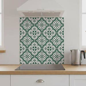 Puede incluir: Revestimiento de cocina decorativo con un patrón repetido de diseños florales verdes y grises sobre un fondo blanco. Las baldosas están instaladas encima de una placa de cocina negra y debajo de una campana extractora blanca.