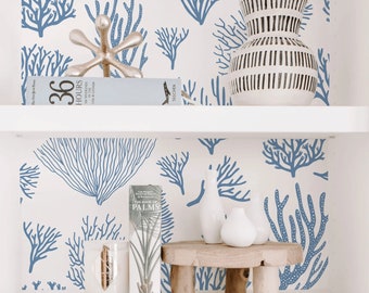 May include: A white shelf with blue coral-patterned wallpaper. Decorative items include a gold metal jack, a book titled "36 Hours", a black and white striped vase, a wooden pedestal, white vases, a candle, and a book titled "The Book of Palms".