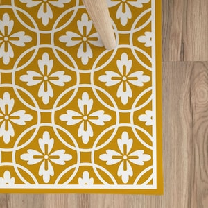 May include: A yellow and white patterned floor mat with a geometric design. The mat features a repeating pattern of white flowers and circles on a mustard yellow background.