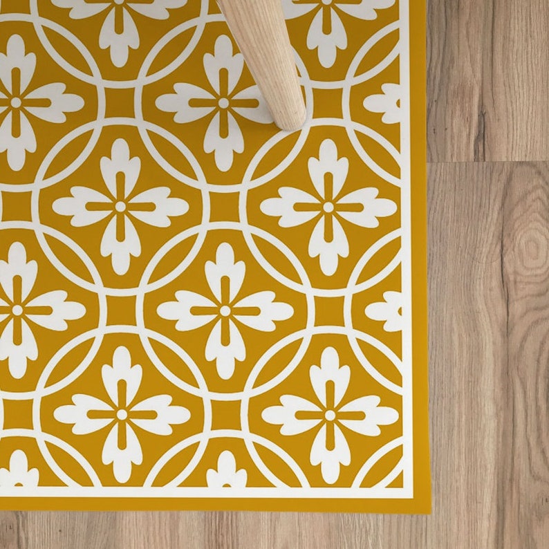 May include: A yellow and white patterned floor mat with a geometric design. The mat features a repeating pattern of white flowers and circles on a mustard yellow background.