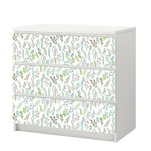 May include: White dresser with three drawers featuring a floral pattern of green and blue leaves and red berries on the front of each drawer.