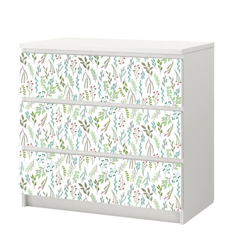 May include: White dresser with three drawers featuring a floral pattern of green and blue leaves and red berries on the front of each drawer.