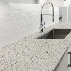 May include: A kitchen countertop with a speckled pattern in shades of white, gray, blue, and gold. A stainless steel sink and faucet are installed. White subway tile backsplash.