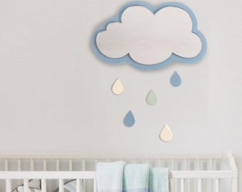 May include: A blue cloud-shaped mirror with a silver reflective surface and five blue, green, and cream raindrops hanging below. The mirror is mounted on a white wall above a white crib.