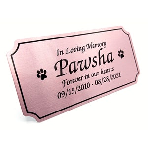 May include: A pink metal plaque with black text that reads "In Loving Memory Pawsha Forever in our hearts 09/15/2010 - 08/28/2021". There are two paw prints on either side of the text.