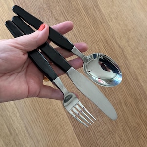 Può includere: Un set di tre posate d'argento con manici in plastica nera. Il set comprende una forchetta, un coltello e un cucchiaio.