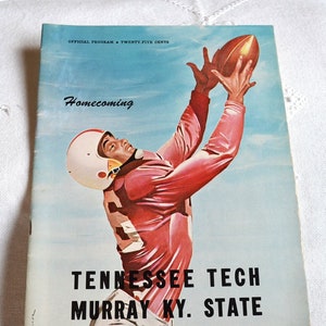 May include: Vintage football program cover featuring a player in a red uniform reaching for a brown football against a blue sky. The cover reads "Homecoming" and lists "Tennessee Tech Murray Ky. State" with the date "October 26, 1957". The program is marked "Official Program Twenty-Five Cents".