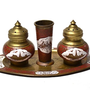 May include: A vintage brass and enamel condiment set featuring two lidded shakers and a tall vase, all resting on a matching tray. The set has a red and white floral design with gold accents. The tray measures approximately 8 inches long.