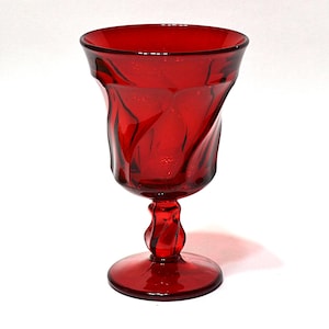 May include: A ruby red glass goblet with a twisted stem and a flared, textured bowl. The glass has a glossy finish and is set against a white background. The goblet is likely for serving beverages.