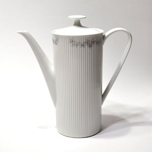 May include: A tall white porcelain coffee pot with a cylindrical body featuring vertical ribbed textures. The upper rim is decorated with a delicate grey floral pattern. It includes a matching lid with a small knob handle and a curved spout.