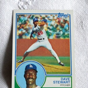 May include: A vintage Topps baseball card featuring Dave Stewart of the Los Angeles Dodgers. The card shows Stewart pitching in his Dodgers uniform, with a portrait of him in a blue cap. The card has a green border and the Topps logo.