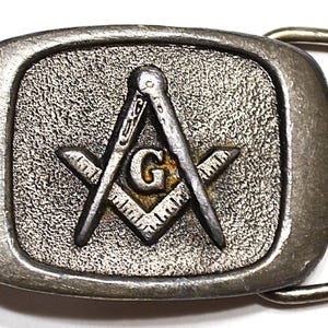 May include: Silver-toned belt buckle with a Masonic symbol, featuring a compass and square with a 'G' in the center.
