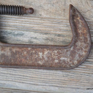 May include: A rusty metal C-clamp with a threaded screw. The clamp has a faded inscription that reads "Made in USA".