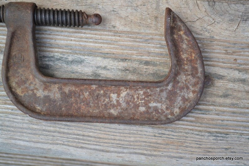 May include: A rusty metal C-clamp with a threaded screw. The clamp has a faded inscription that reads "Made in USA".