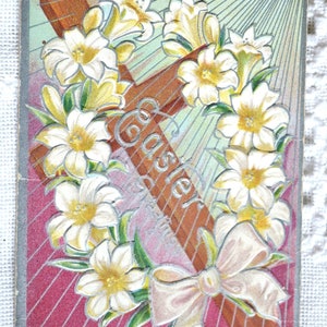 May include: Vintage Easter greeting card featuring a brown cross adorned with white lilies and a cream-colored bow. The word "Easter" is written diagonally across the cross. The background has a pink and green color scheme.