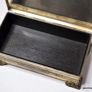 May include: A rectangular jewellery box with a gold-coloured exterior and a black interior. The box has ornate detailing on the feet and edges, and the lid is open, revealing a mirrored surface. Likely vintage.