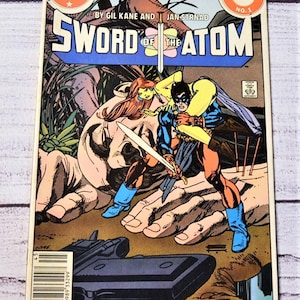 May include: A vintage comic book titled "Sword of the Atom" from 1984. The cover features a dynamic illustration of two figures in combat, with a sword and a large hand in the background. The DC Comics logo is visible.