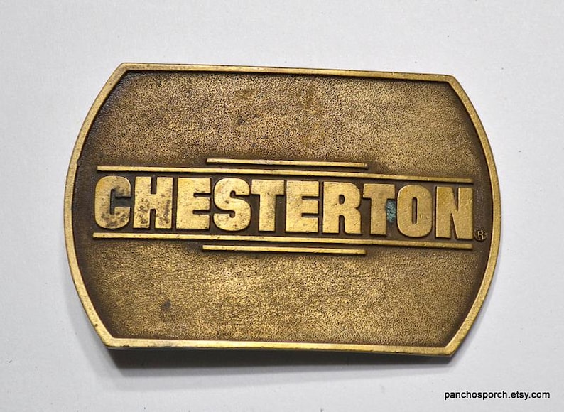 May include: A vintage brass belt buckle with the name "CHESTERTON" in bold, raised letters. The buckle has a rectangular shape with rounded edges and a weathered, antique finish. The text is centered on the buckle.