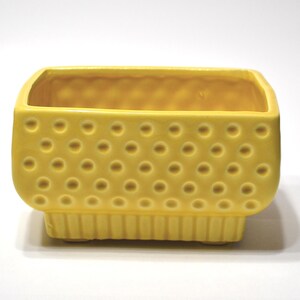 May include: A rectangular yellow ceramic planter featuring a textured exterior with a raised polka dot pattern on the upper section and vertical ribbed detailing along the base, providing a structured and uniform appearance for this small container.
