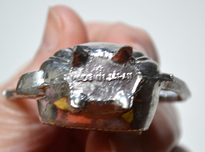 May include: A silver-colored metal object with a textured surface. The object has a rounded shape with two protruding elements and the text "MADE IN JAPAN" is visible.