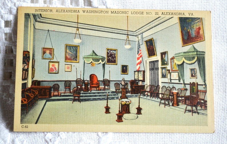 May include: A vintage postcard depicting the interior of the Alexandria Washington Masonic Lodge No. 22 in Alexandria, Virginia. The lodge room features a raised platform with a red throne, surrounded by wooden chairs and a large American flag. The walls are adorned with framed portraits and paintings.