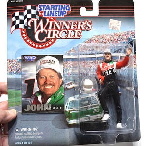 May include: A Starting Lineup Winners Circle action figure of John Force in a racing suit. The figure is in a plastic package with a picture of John Force and a race car. The packaging includes the text "Starting Lineup" and "Winners Circle".