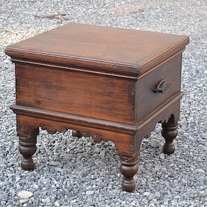 May include: A dark brown wooden side table with a square top and ornate carved details. The table has a decorative handle and four turned legs. The table is approximately 24 inches tall.