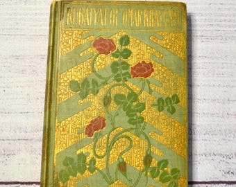 Könnte beinhalten: Ein antikes Buch mit dem Titel "Rubaiyat of Omar Khayyam". Das Cover ist gold und grün mit roten Rosen und grünen Blättern. Das Buch hat einen verzierten, dekorativen Einband.