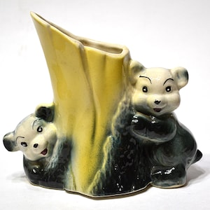 May include: A vintage ceramic vase in the shape of a tree trunk with two bear cubs. The vase is primarily yellow with dark green and black accents. The bears are light gray with black eyes and noses. A charming decorative piece.