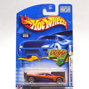 May include: A Hot Wheels die-cast toy car on a blue and white card. The car is orange and purple, labelled "HW Prototype 12". The card features the Hot Wheels logo, the text "Race & Win Online", and the number "036".