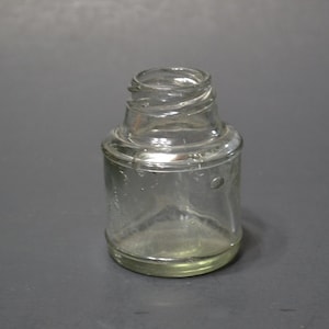 May include: A clear glass bottle with a textured surface and a rounded bottom. The bottle has a small opening at the top.