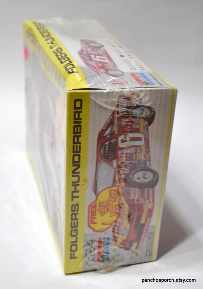Puede incluir: Un modelo en caja de un coche de carreras Folgers Thunderbird. La caja es amarilla y presenta im&aacute;genes del coche en rojo, blanco y azul. La caja est&aacute; envuelta en pl&aacute;stico transparente.
